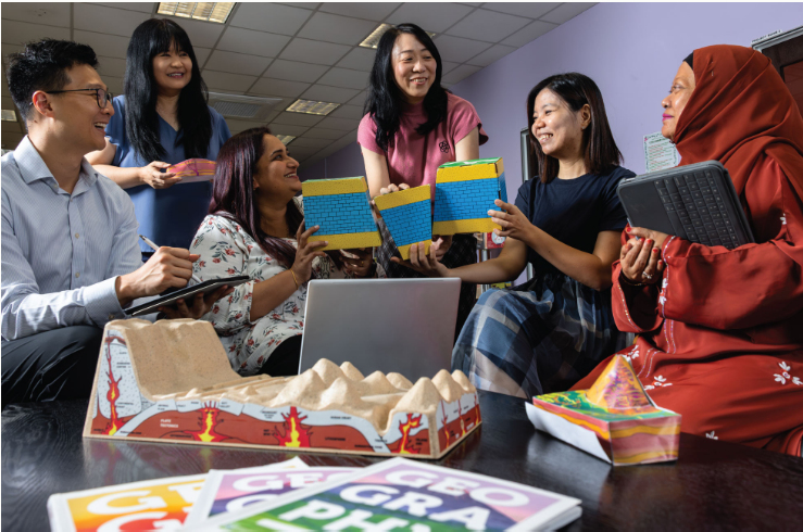 Mdm Emmeline Tay and five fellow educators gathered around a table, discussing colourful Geography teaching models and learning resources.